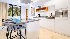A modern kitchen with a central island, bar stools, a microwave, and a window with a view of trees. - 2BR Condo Beautiful Common Areas, Sleeps 6! (Akumal)