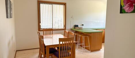 A dining area with a wooden table and chairs, a kitchen counter, and a window with blinds.