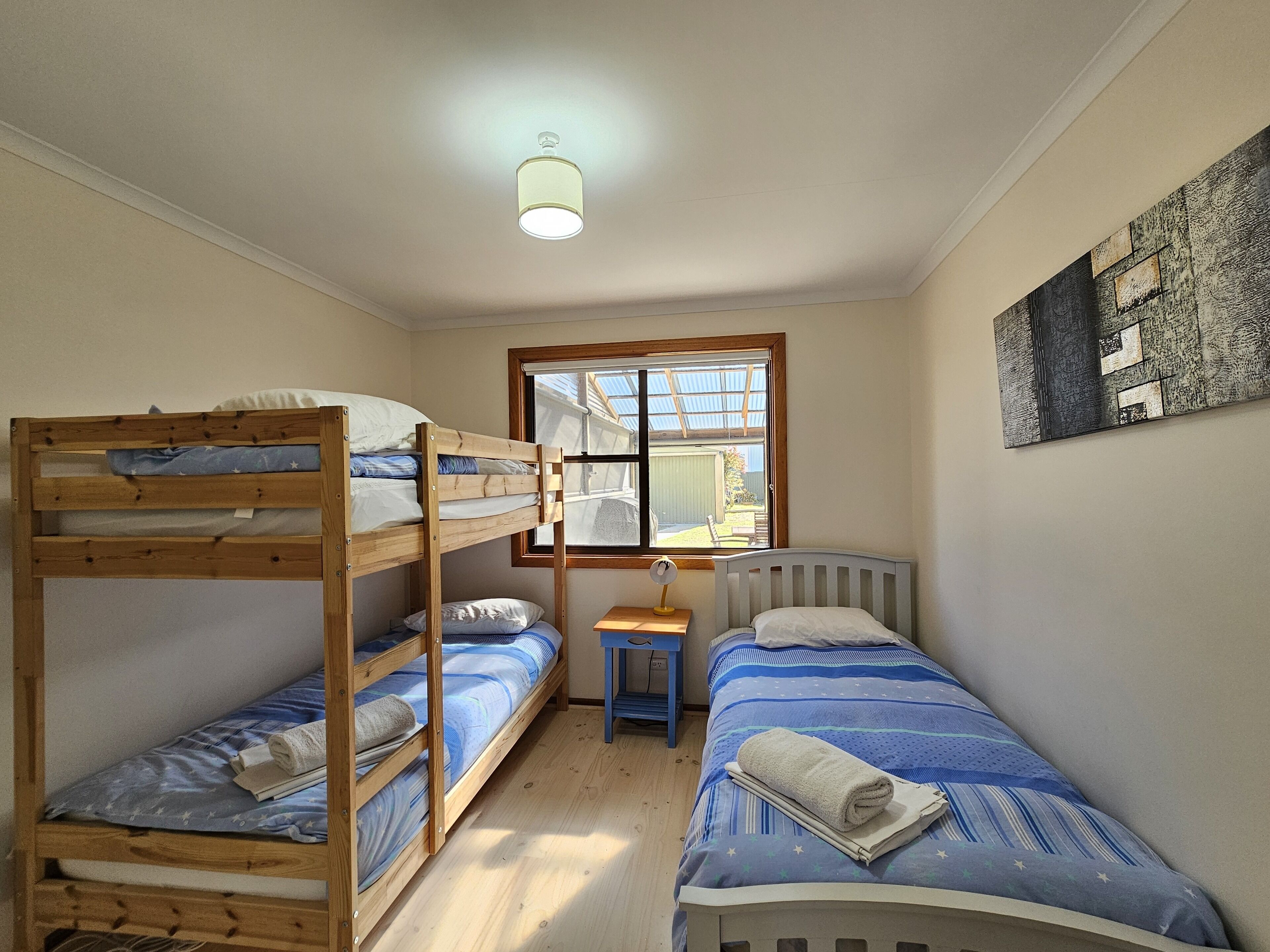 A dormitory room with bunk beds, a small table, a lamp, and a window with a view of the outside.