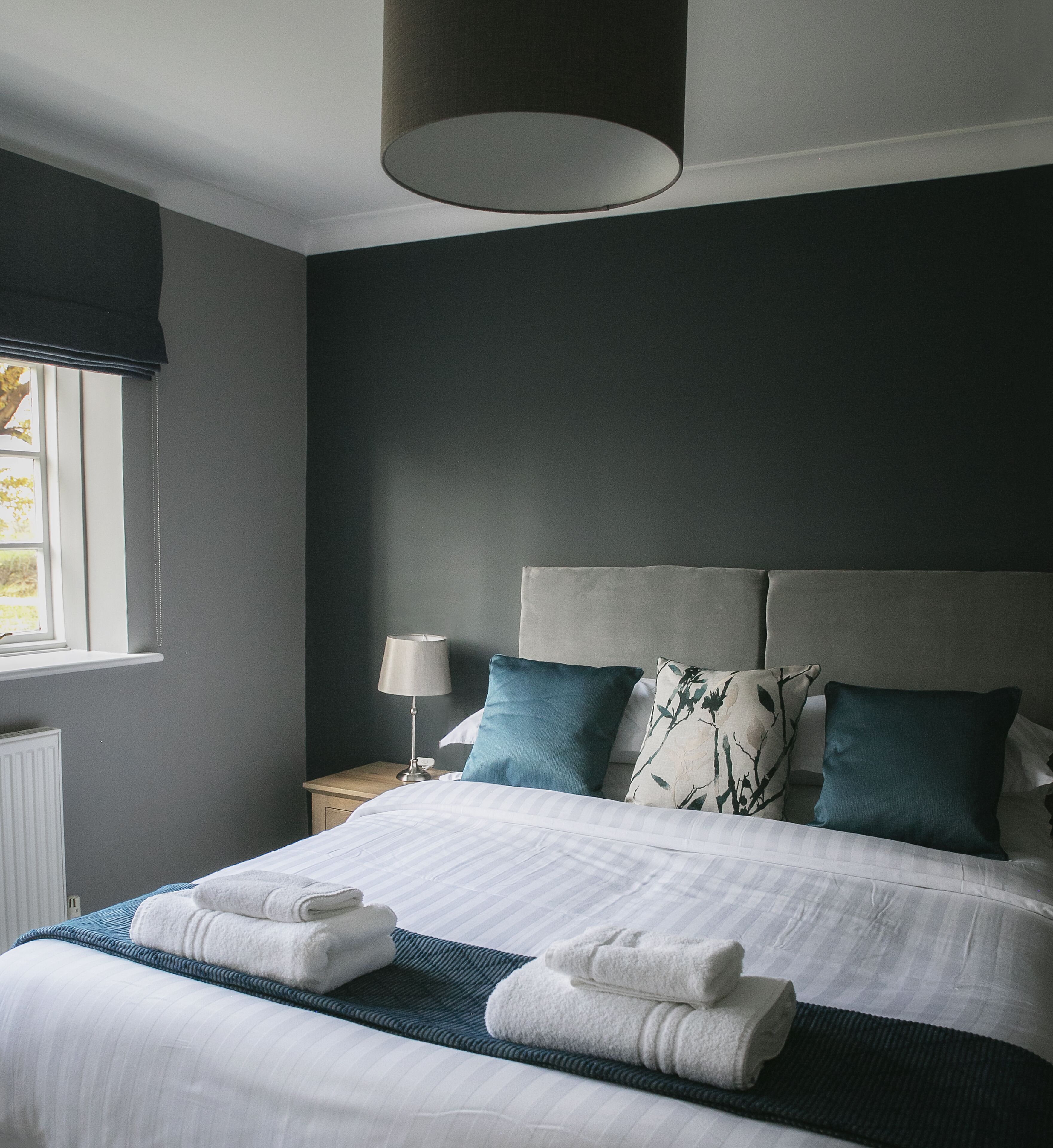 A modern bedroom with a large bed, dark walls, and a window with blinds.
