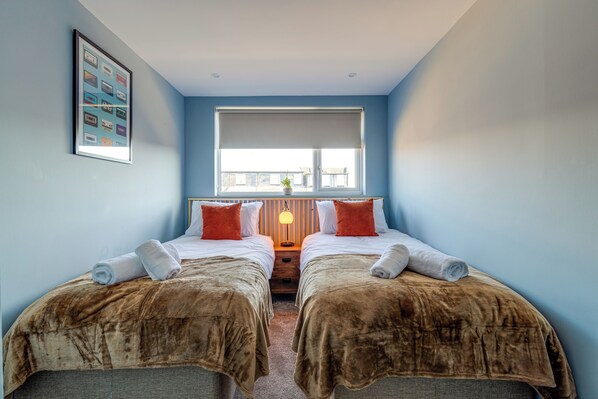 A twin bedroom with two beds, a large window, and a framed picture on the wall.