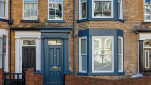 A corner terraced house with a dark blue front door, white-framed windows, and a brick facade.