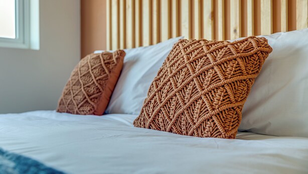 A bed with white bedding and two decorative pillows with a woven pattern.