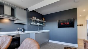 A modern kitchen with grey cabinets, a white countertop, and a built-in oven. There is a coffee maker, a kettle, and a sink. A Netflix sign is displayed on the wall.