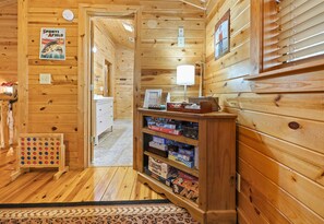 L’intérieur d’une cabane en bois, avec une étagère en bois où sont rangés des jeux de société, un tableau encadré accroché au mur et une porte donnant sur une autre pièce.
