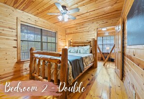Une chambre dans une cabane en bois, avec un lit, un ventilateur de plafond et de grandes fenêtres.