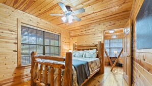 A wooden cabin bedroom with a bed, a ceiling fan, and large windows. - Pet-Friendly Playset Retreat for Families (Broken Bow)