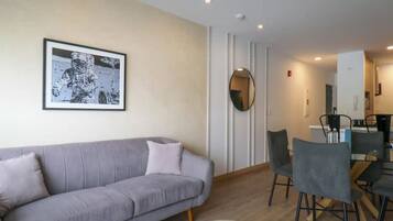 Ein Wohnzimmer mit grauem Sofa, einem Esstisch mit Stühlen und einem gerahmten Bild an der Wand.