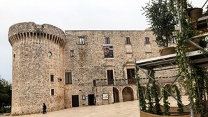 Un edificio histórico de piedra con una torre redonda, arcos en las puertas y un patio interior.