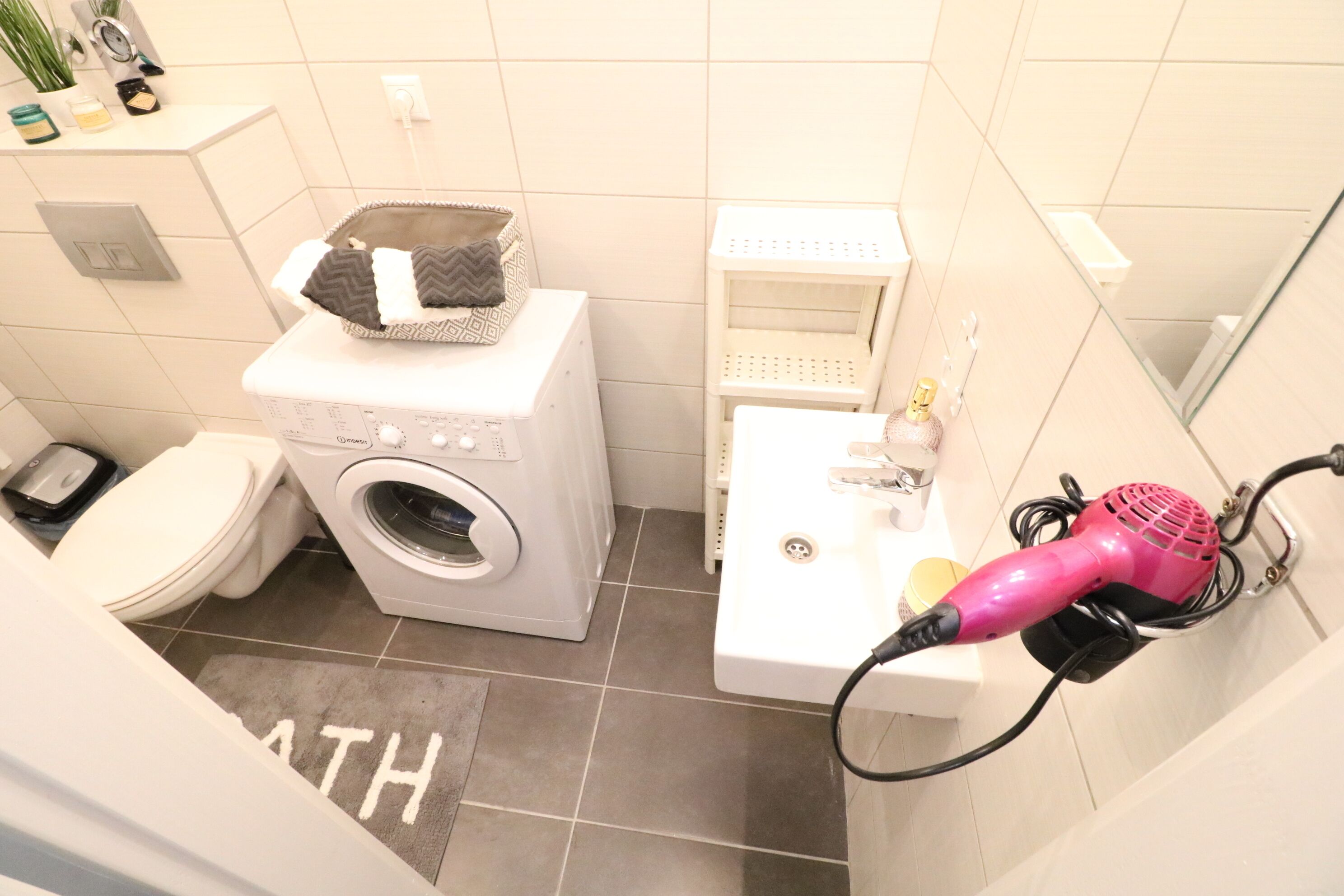 Een kleine badkamer met een wasmachine, toilet, wastafel en haardroger.