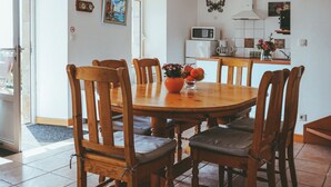 Ein Essbereich mit einem Holztisch und Stühlen, im Hintergrund eine Küche und eine Tür, die nach draußen führt.
