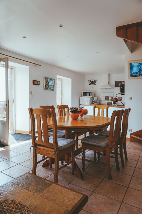 Zona pranzo con tavolo e sedie in legno, cucina sullo sfondo e una porta che dà all'esterno.