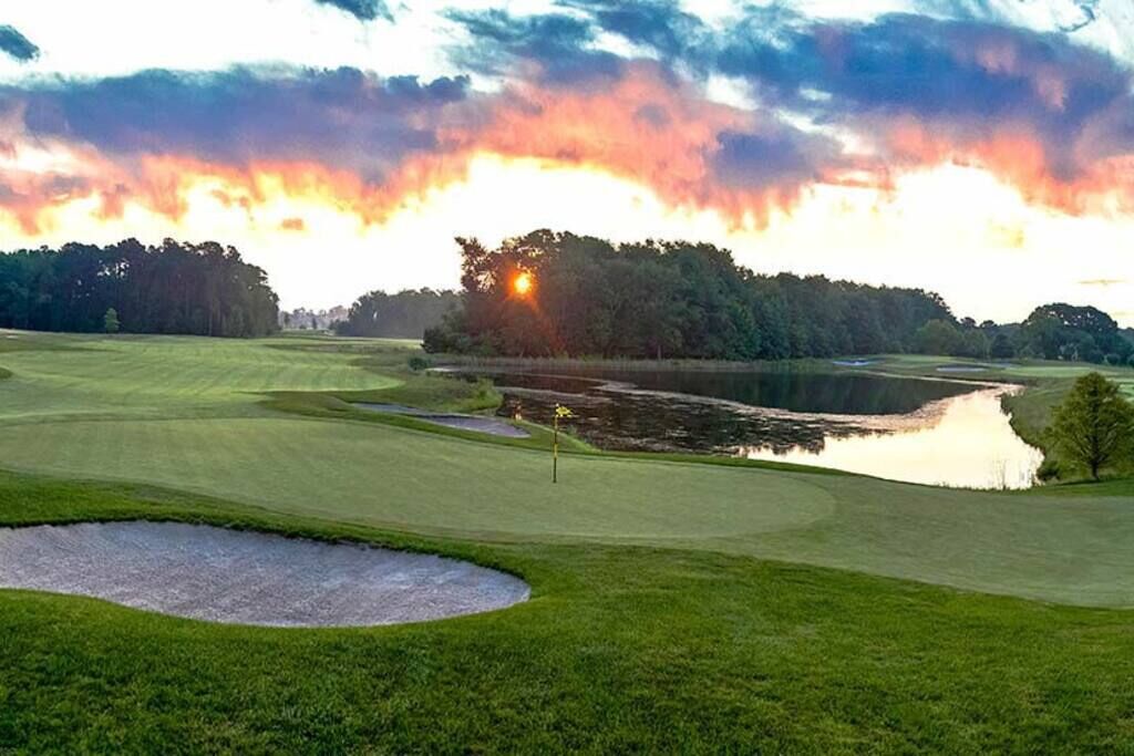 Ein Golfplatz mit Teich, Bäumen und Sonnenuntergang.