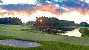 Un parcours de golf avec un étang, des arbres et un coucher de soleil.