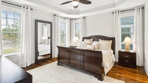 Une chambre à coucher avec un lit en bois foncé, du linge de lit blanc, un grand miroir et un ventilateur de plafond.