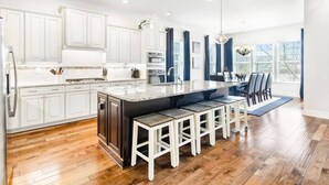 Une cuisine moderne avec des meubles blancs, un grand îlot central doté de tabourets, et un coin repas offrant une vue agréable.