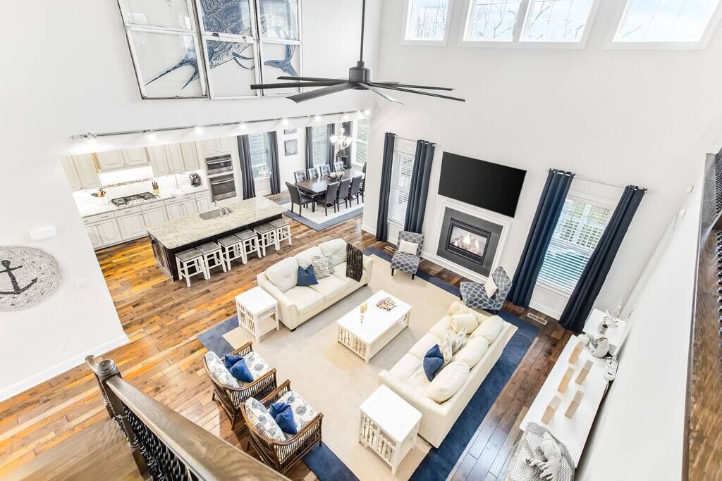 A spacious living area with a high ceiling, a fireplace, and a dining area with a kitchen in the background.