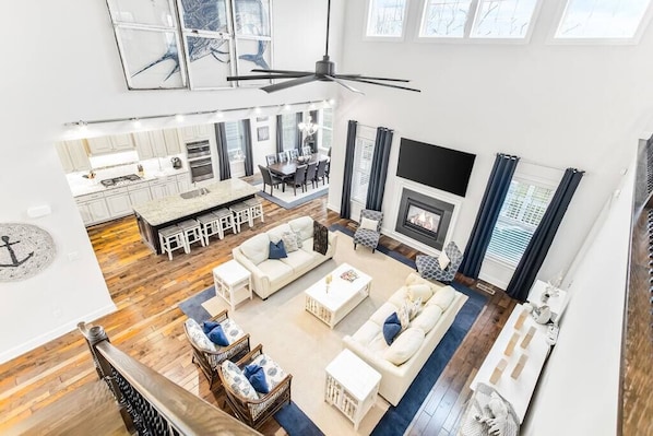 A spacious living area with a high ceiling, a fireplace, and a dining area with a kitchen in the background.