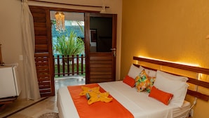 Habitación de hotel con cama, cabecera de madera, una mesita y vista a un jardín a través de una puerta abierta.