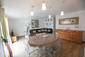 Een moderne keuken met een houten eettafel, transparante stoelen, een zwarte bank en hanglampen.