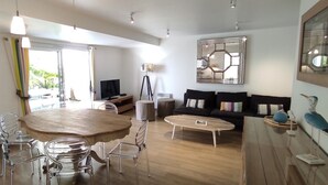 Un salon moderne avec une table à manger en bois, des chaises transparentes, un canapé et un grand miroir.
