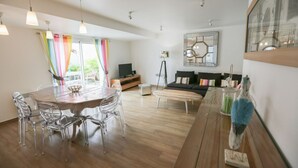 Un salon moderne avec une table à manger en bois, des chaises transparentes, un canapé noir et une table basse en verre.