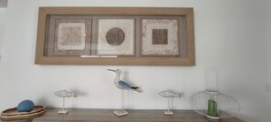 Un mur orné de trois œuvres d’art encadrées et, en dessous, une étagère en bois sur laquelle sont exposées des sculptures d’oiseaux et de poissons.
