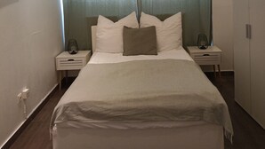 A modern bedroom with a large bed, two bedside tables, and a wardrobe.