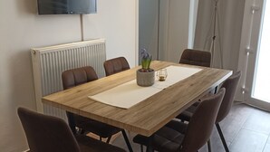 A modern dining area with a wooden table, six chairs, a potted plant, and a flat-screen TV mounted on the wall.