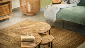 A cozy living room with a wooden coffee table, a woven rug, a large vase, and a green sofa with a hat on it. - Prime location Sunny 3bedroom apartment (Tel Aviv)