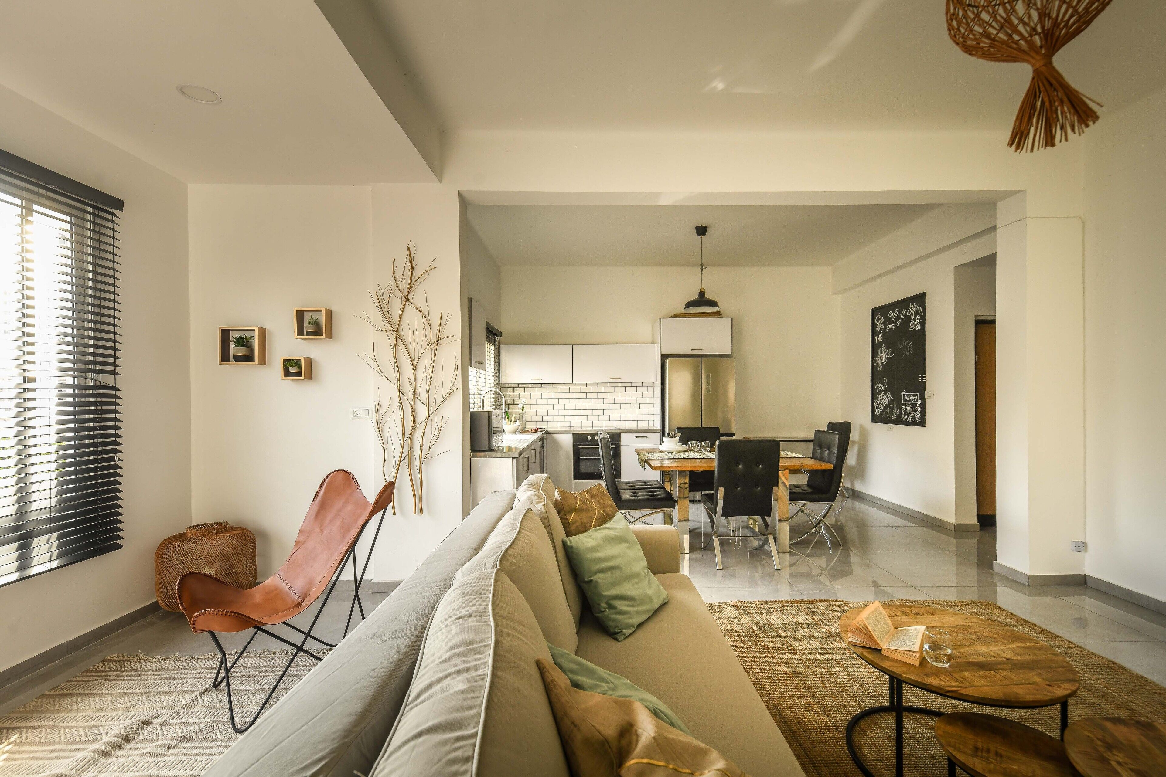 A modern living room with a sofa, a dining area with a table and chairs, and a kitchen in the background.