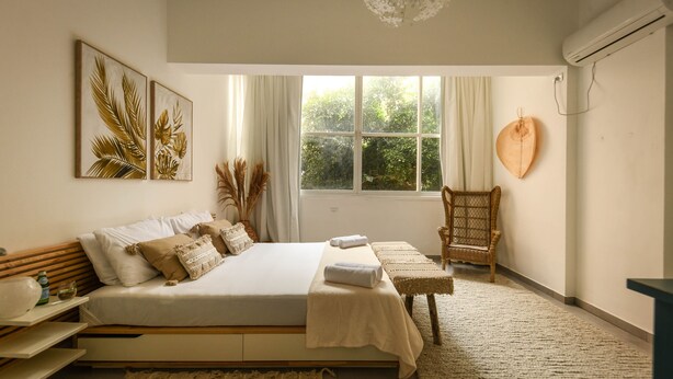 A bedroom with a bed, a chair, a window, and a wall-mounted air conditioner. - Prime location Sunny 3bedroom apartment (Tel Aviv)