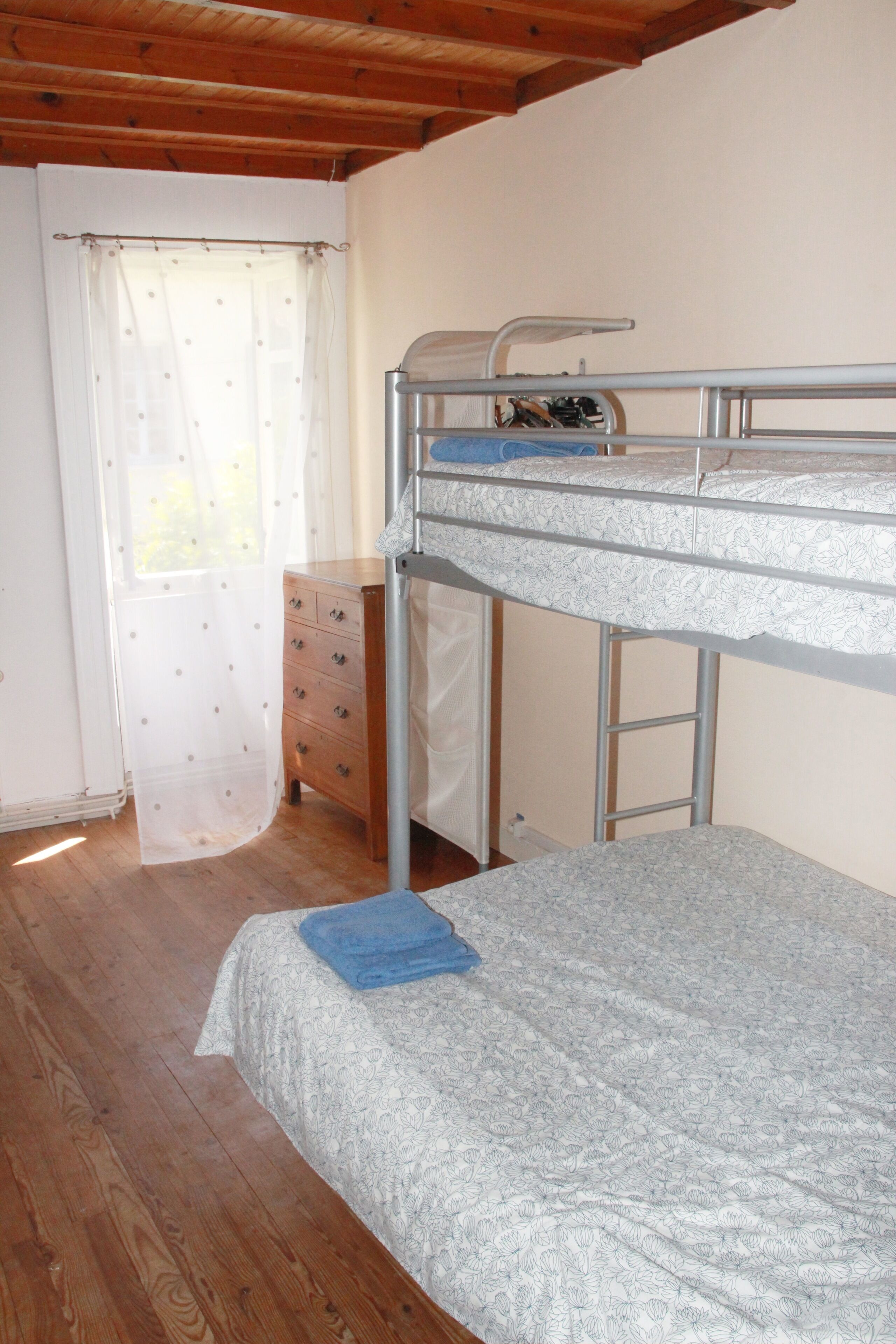 Habitación con literas, piso de madera, cómoda y ventana con cortinas traslúcidas.