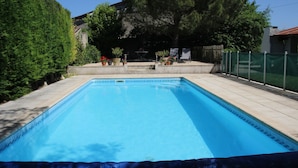 Une piscine rectangulaire avec une terrasse carrelée, entourée de plantes en pot et d’une clôture en bois.