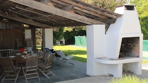 Une terrasse extérieure avec une table et des chaises en bois, un four en briques et un espace salon abrité.