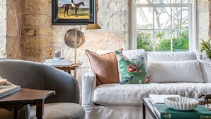 Un accogliente soggiorno con parete in pietra, un quadro con un cavallo, un'ampia finestra e un divano bianco con cuscini colorati.