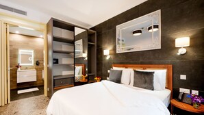 Een moderne hotelkamer met een groot bed, een kaptafel met spiegel, een inbouw kast en een nachtkastje met lamp.