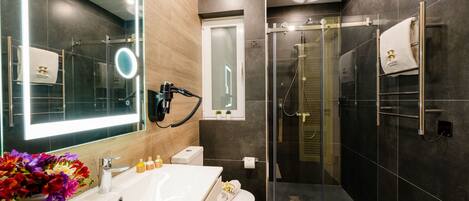 Un baño moderno con un espejo grande, una ducha con cerramiento de vidrio, un inodoro y un lavamanos con artículos de aseo.