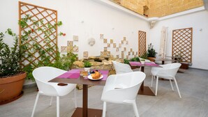Een patio met witte rieten stoelen, een tafel met een bord eten, en een decoratieve muur met tegels en planten.
