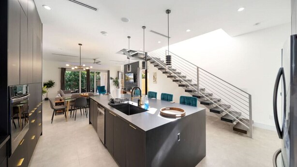 Une cuisine moderne dotée d’un îlot central, d’un coin repas avec une table et des chaises, et d’un escalier menant à un niveau supérieur.