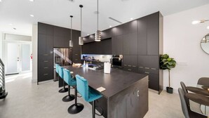 Une cuisine moderne dotée d’un îlot central, de tabourets de bar et de luminaires suspendus.