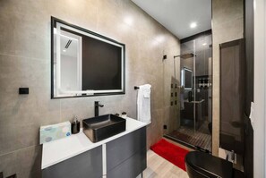Une salle de bain moderne avec un grand miroir, un lavabo noir et une douche à parois de verre.