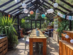 A covered patio area with a wooden table and chairs, surrounded by potted plants and a 'Happy Birthday' banner. - The Bull Pen (Colyton)