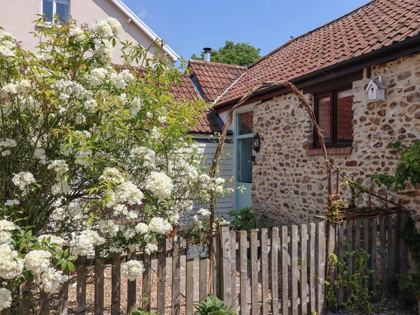 A stone house with a tiled roof, a wooden fence, and white flowering bushes. - The Bull Pen (Colyton)