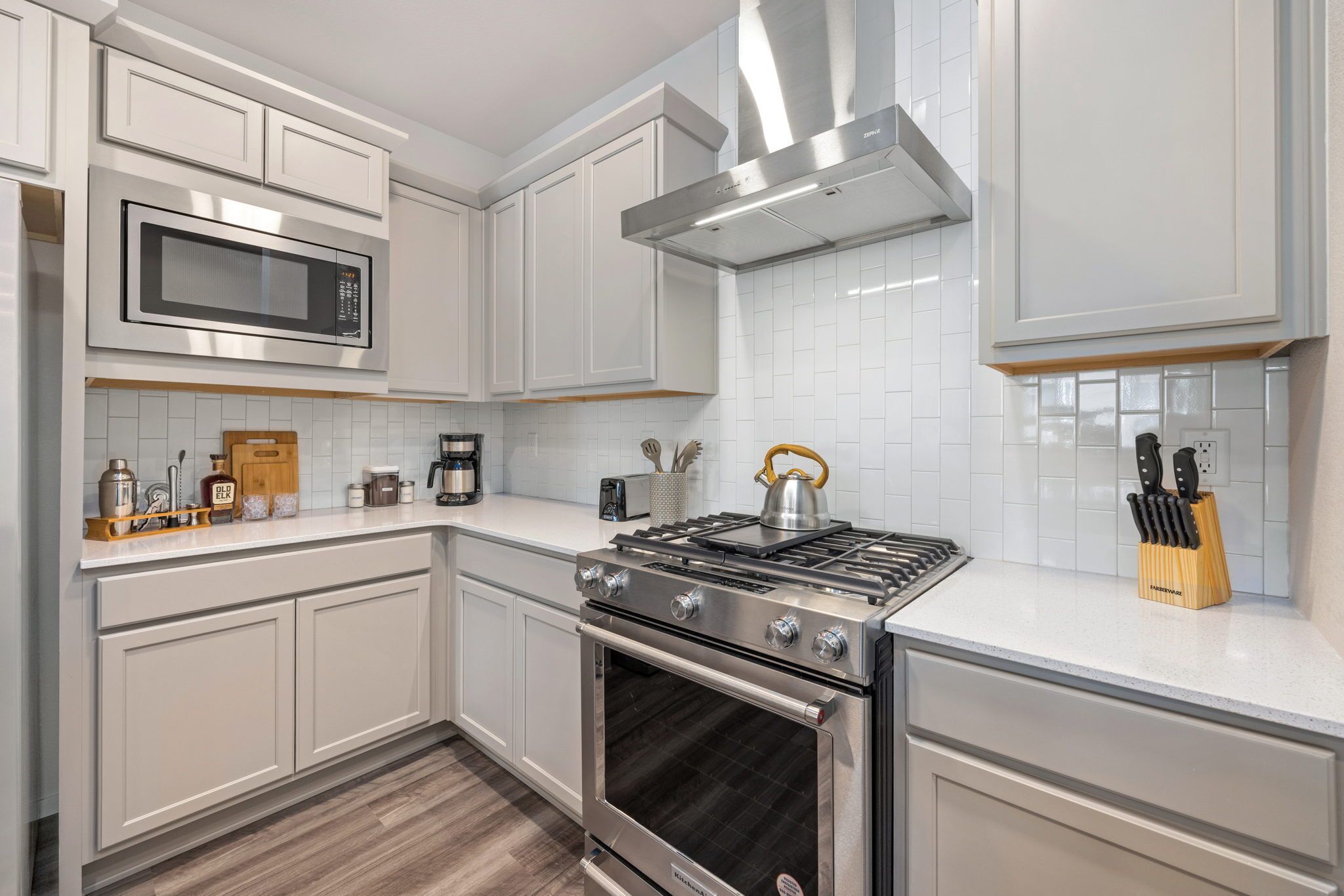 A modern kitchen with white cabinetry, a stainless steel stove, a microwave, and a built-in oven.