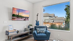 A living room with a large window, a blue armchair, a guitar, a bookshelf, and a painting of the Eiffel Tower. - Stylish Music-Inspired Retreat Near Old Town FC (Fort Collins)