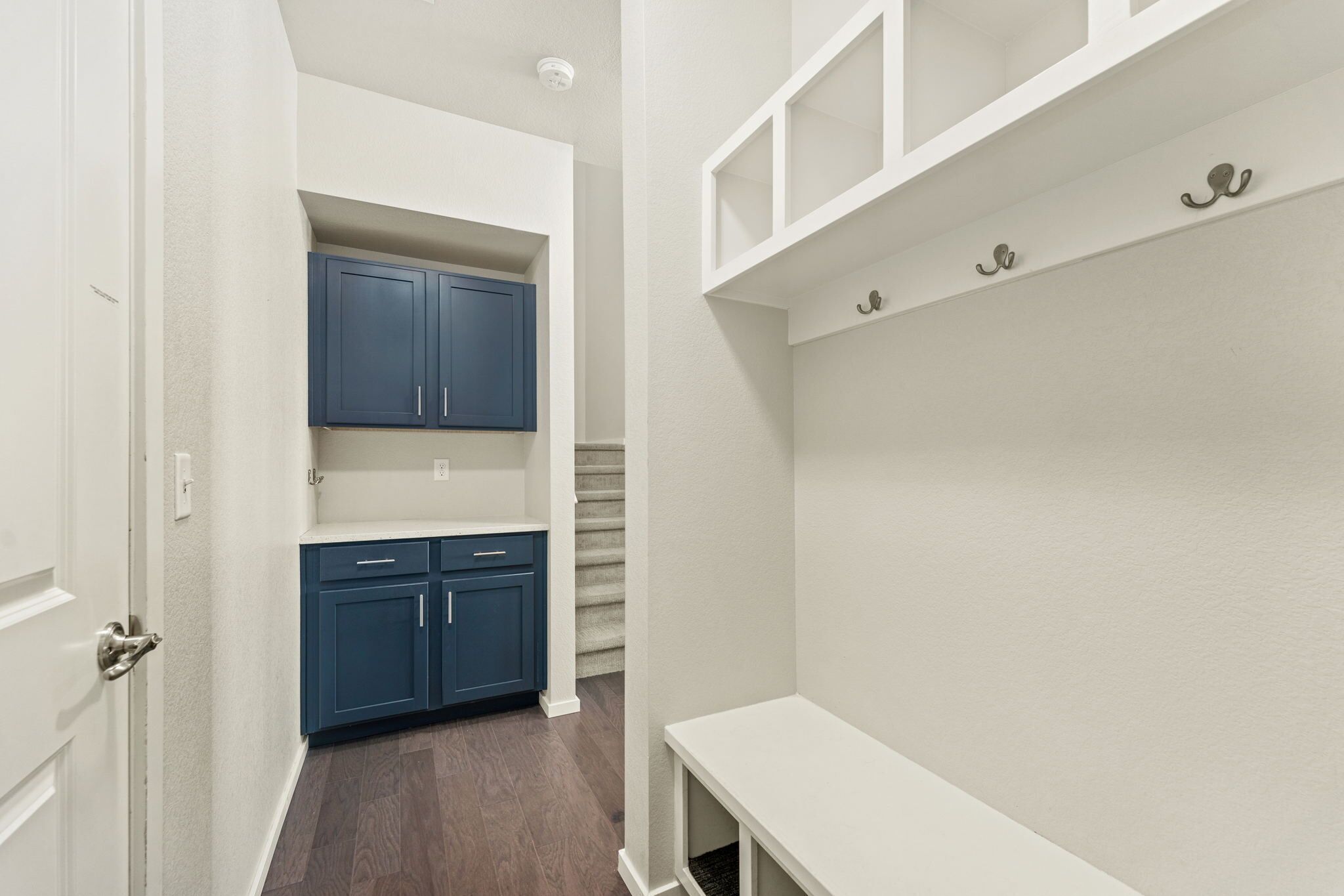 A narrow hallway with a white door, a blue cabinet, and a white bench.