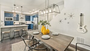 A modern kitchen with blue cabinets, a wooden dining table, and a yellow vase. - Stylish Music-Inspired Retreat Near Old Town FC (Fort Collins)