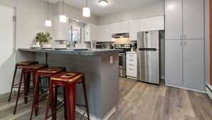 Une cuisine moderne dotée d’un îlot central, d’appareils électroménagers en acier inoxydable et de tabourets de bar en bois.