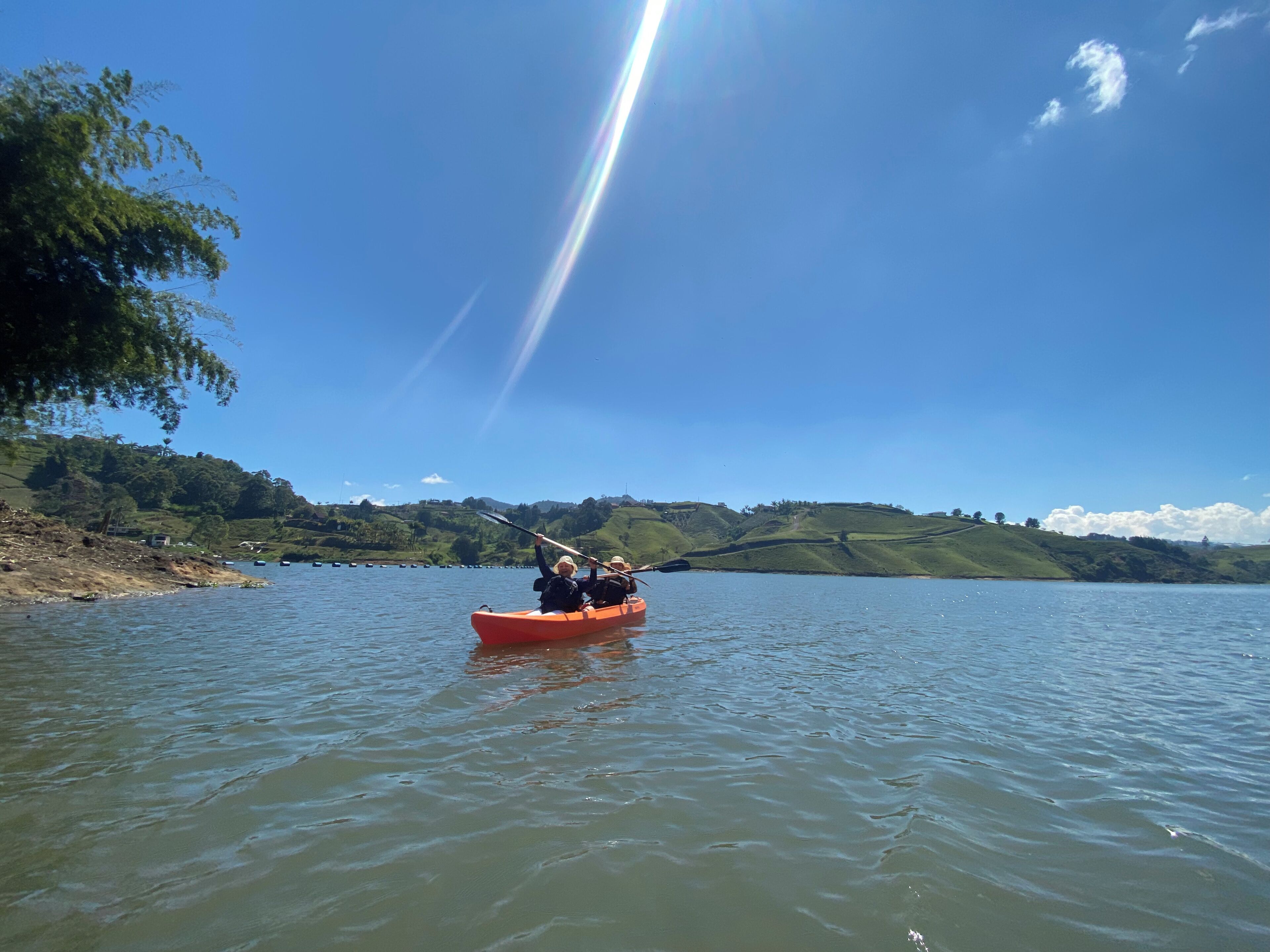 A calm lake with a red kayak in the foreground, surrounded by green hills and clear blue sky.